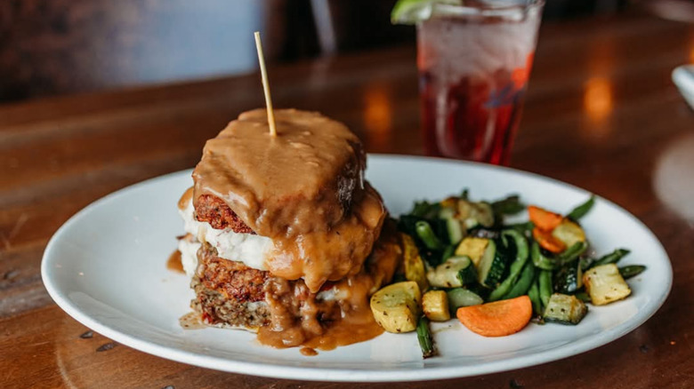 Meatloaf topped with brown gravy and a side of grilled vegetables