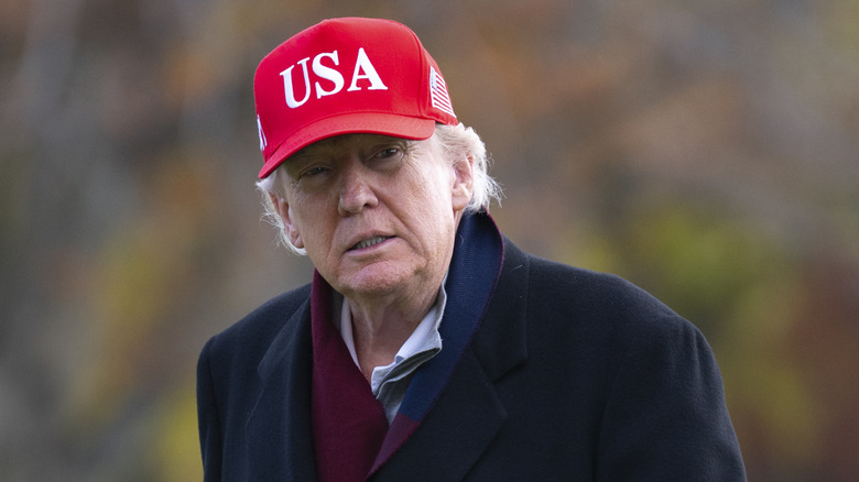President Donald Trump in a red USA hat and black coat outside.