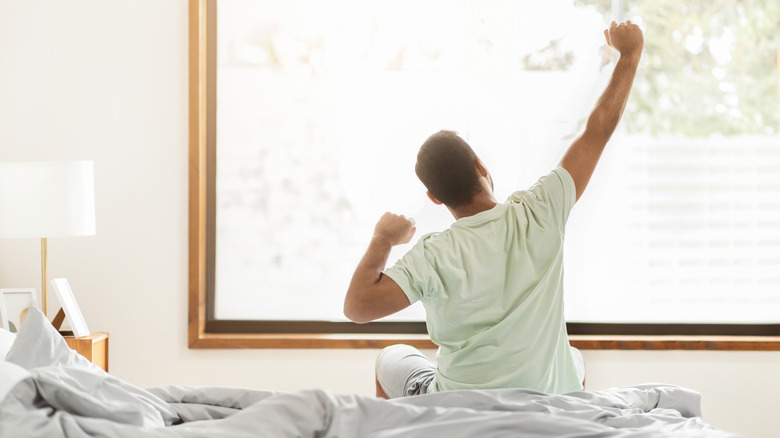 A man stretching as he sits up in bed
