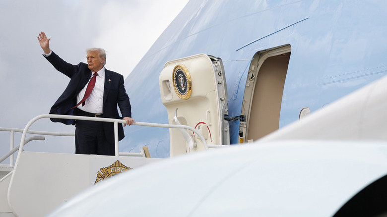 Donald Trump at the top of the stairs from Air Force One, raising his hand in a wave.