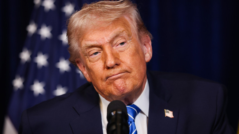 Donald Trump making a pouting expression up close, behind a microphone.