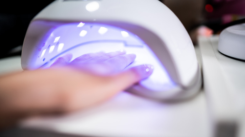A woman's hand with gel nail polish drying inside a UV light chamber