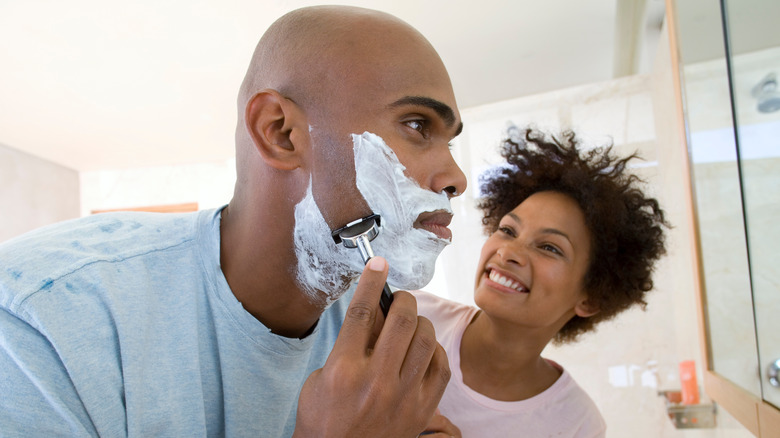 Man shaving face with woman watching
