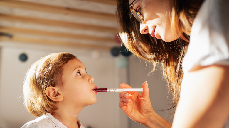 mother administering liquid medication to child