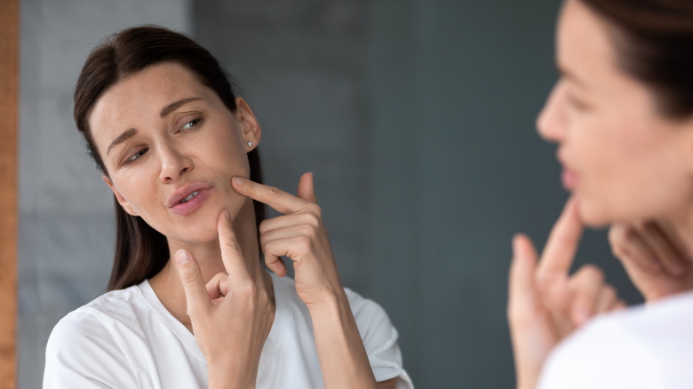 Woman examining a pimple on her face in the mirror