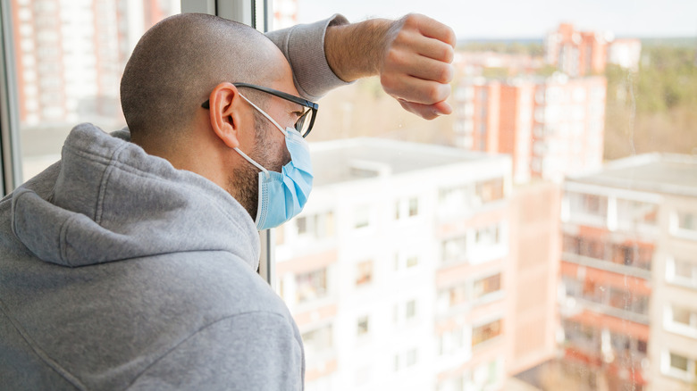 Man alone at a window wearing a mask