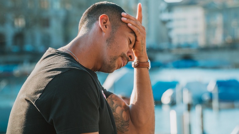 Man sits outside looking stressed with his hand on his forehead