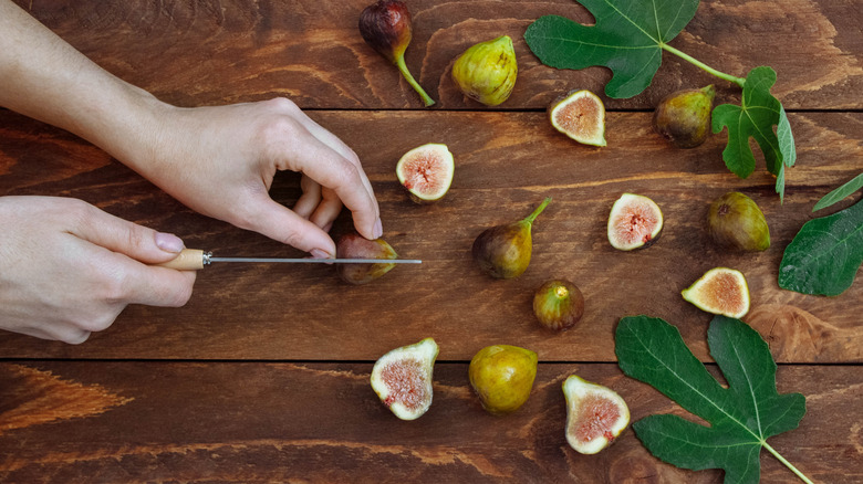 woman cutting figs with green leaves on cutting board