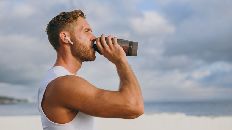A muscular man drinking a protein shake by the beach
