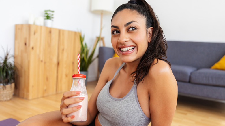 A woman in fitness gear drinking a milk protein shake in a glass bottle with a straw