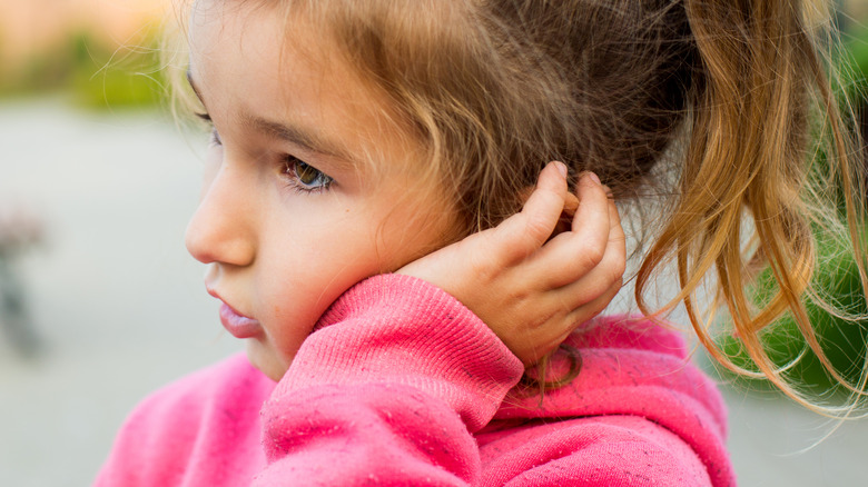 Little girl in pink hoodie holding ear