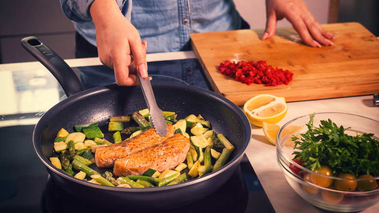 Woman cooking fish with vegetables