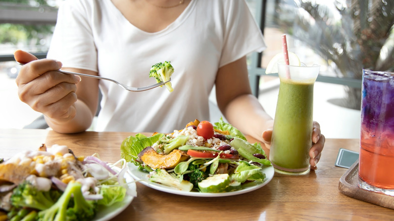Woman is eating a plate of healthy food with broccoli
