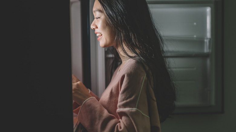 Smiling young woman opening fridge