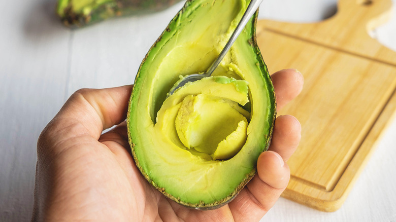 A person serving avocado with a cutting board in the background