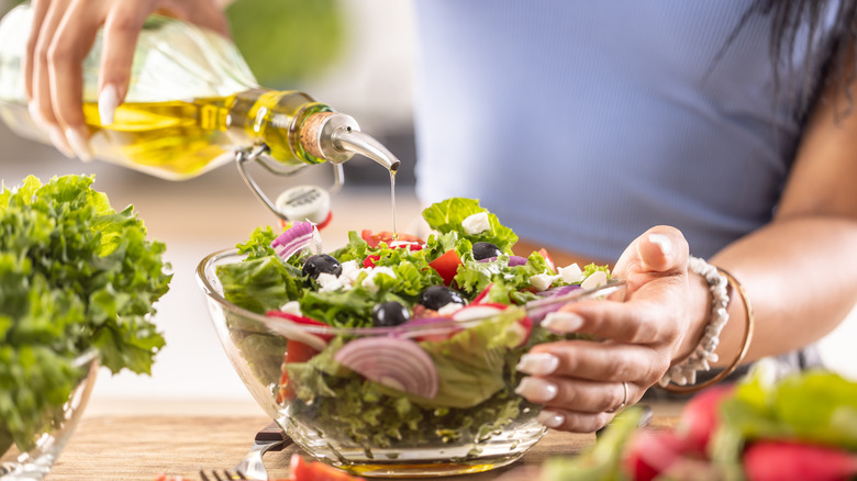 A woman pouring oil over a healthy salad