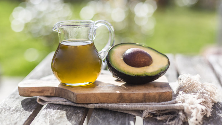 A small glass cruet of avocado oil next to a sliced avocado