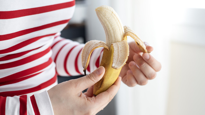 woman's hands peeling back the skin of a banana