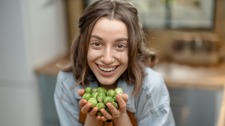smiling woman holding handful of Brussels sprouts