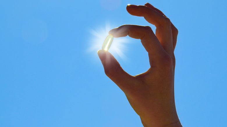 holding vitamin D capsule to sky