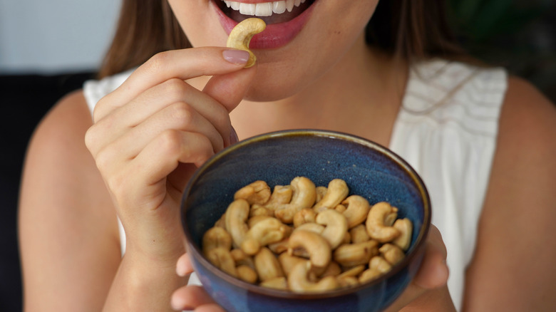 A woman eating a cashew while holding a bowl of cashews