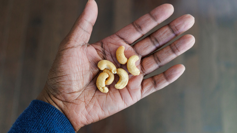 A man's hand holding some cashews