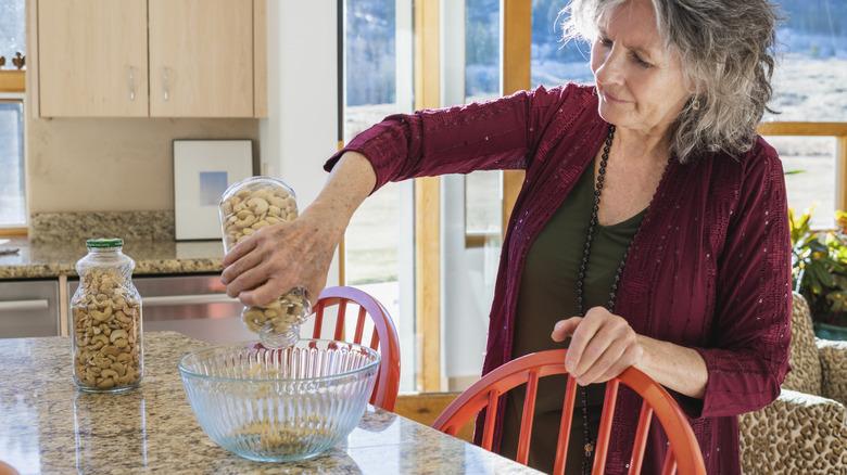 A woman pouring a jar of cashews into a glass bowl