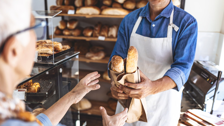 senior woman reaching for fresh bread from clerk