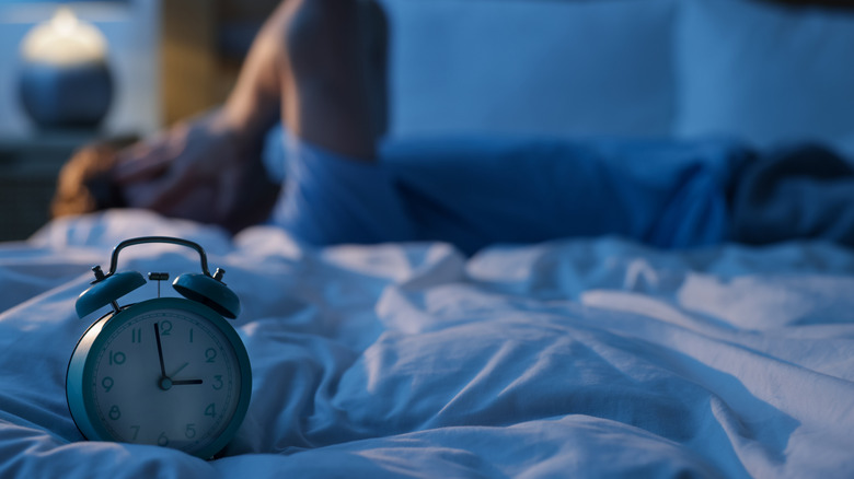 Man with hands on face and alarm clock in foreground