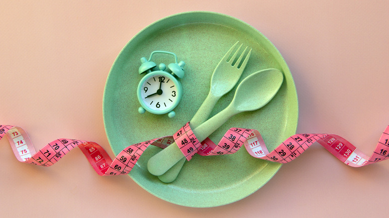 plate, alarm clock, spoon, fork, and measuring tape represent intermittent fasting