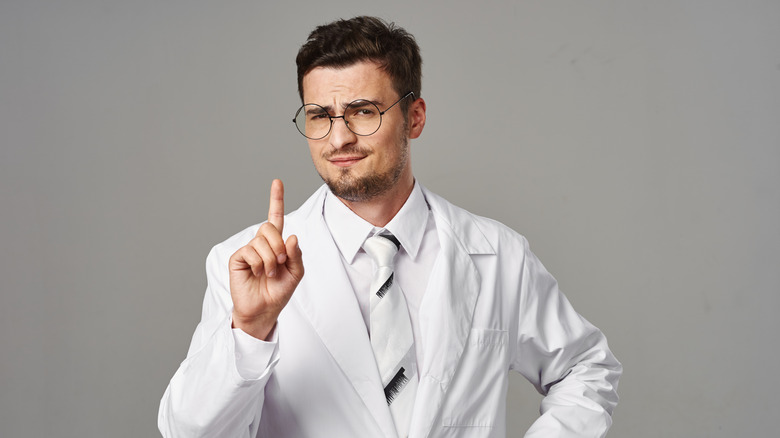 Male in white coat raising finger.