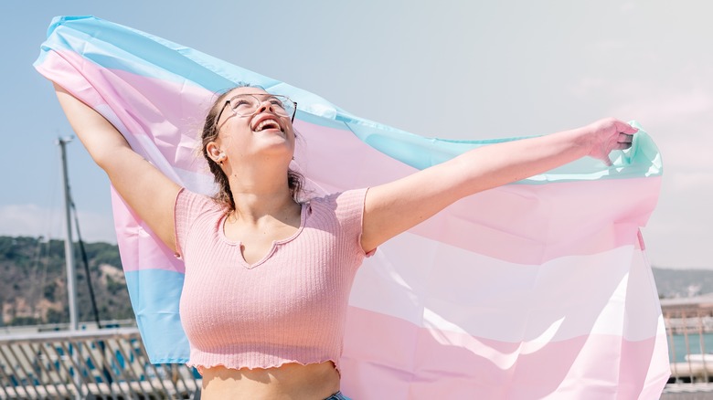trans woman holding up a trans flag