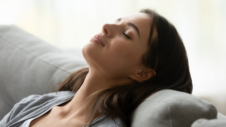 a young woman sits with her head back and eyes closed deep breathing