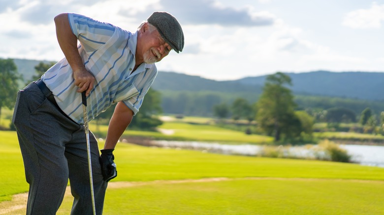 Asian senior man bending to hold painful knee while golfing