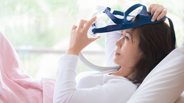 Young woman putting on CPAP mask in bed