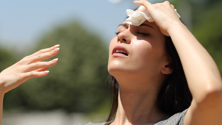 Woman sweating with tissue on forehead