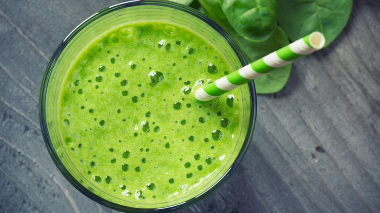 Overhead shot of a spinach smoothie next to spinach leaves