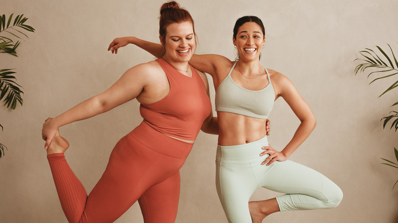 two women standing in workout gear leaning on eachother smiling