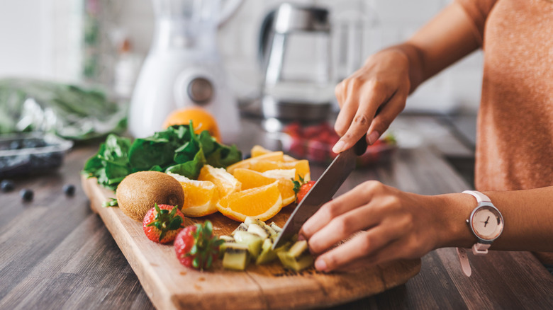 woman in kitchen cutting fruit next to blender
