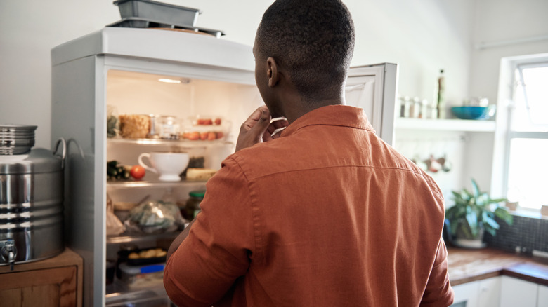 Man thinking in front of open fridge