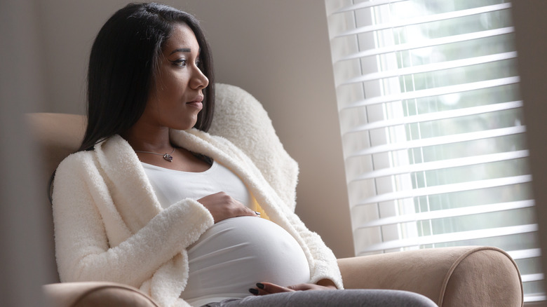Worried pregnant woman looking out window