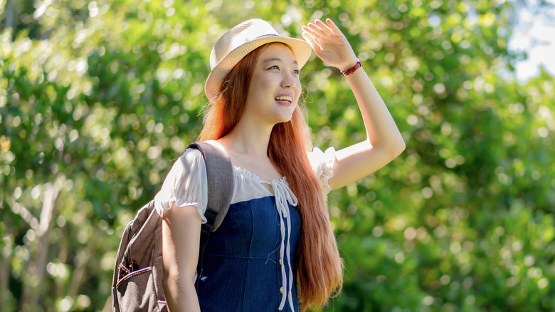 A smiling woman shielding her eyes while walking in the woods