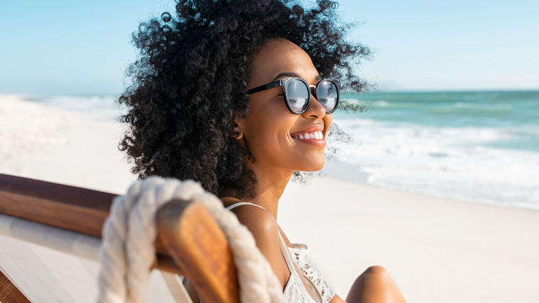 A smiling woman wearing sunglasses sitting on a chair on the beach