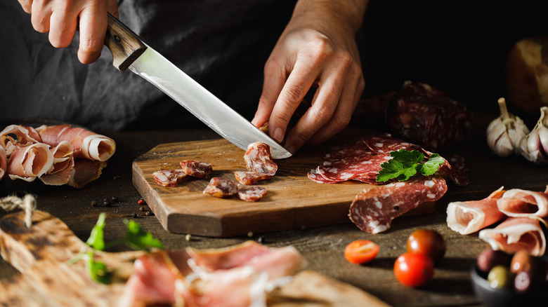hand cutting processed meats on a cutting board