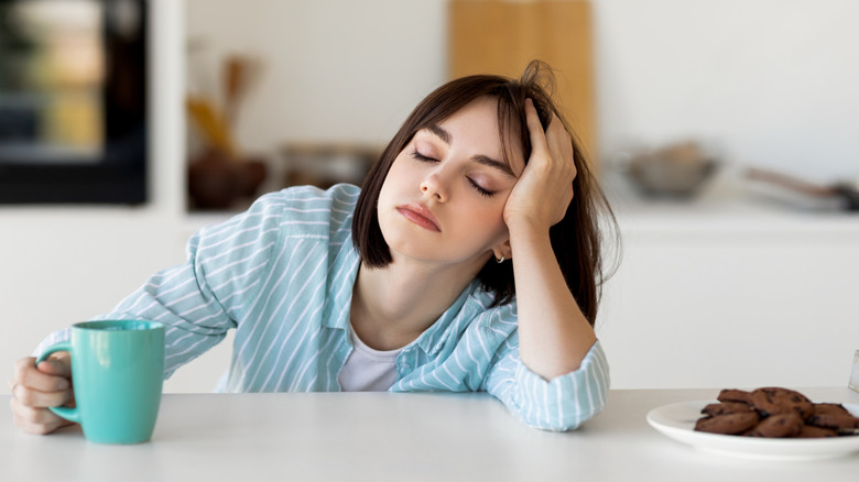 A woman falling asleep at a table with coffee and cookies