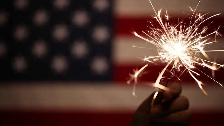 Hand holding sparkler in front of American flag
