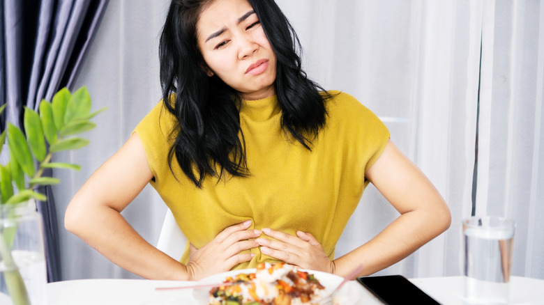woman sitting at table holding stomach in pain