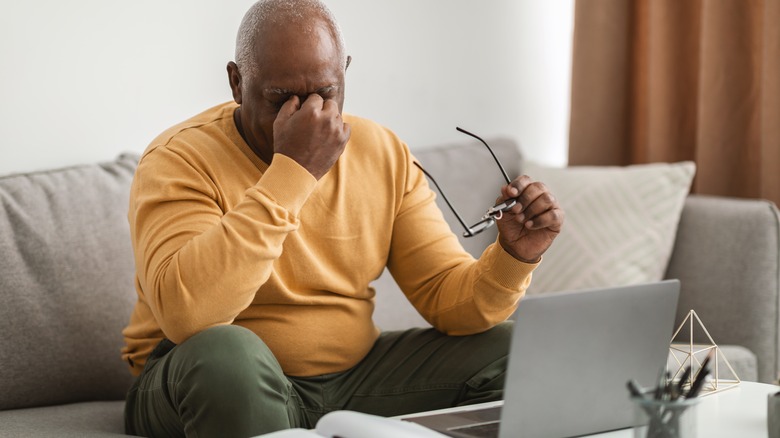 Man sitting on couch with his fingers at the bridge of his nose