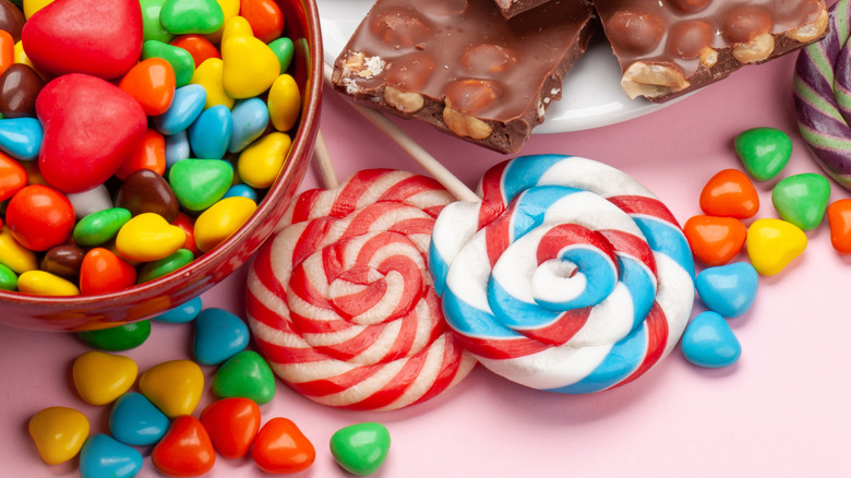 A bowl of candy next to a plate of chocolate bars, lollipops, and loose candies