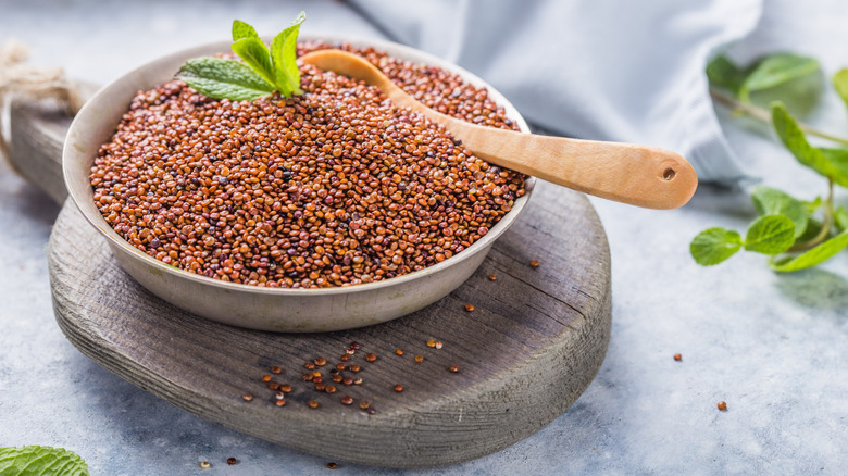 A bowl that contains quinoa and a wooden spoon on top of a wooden cutting board